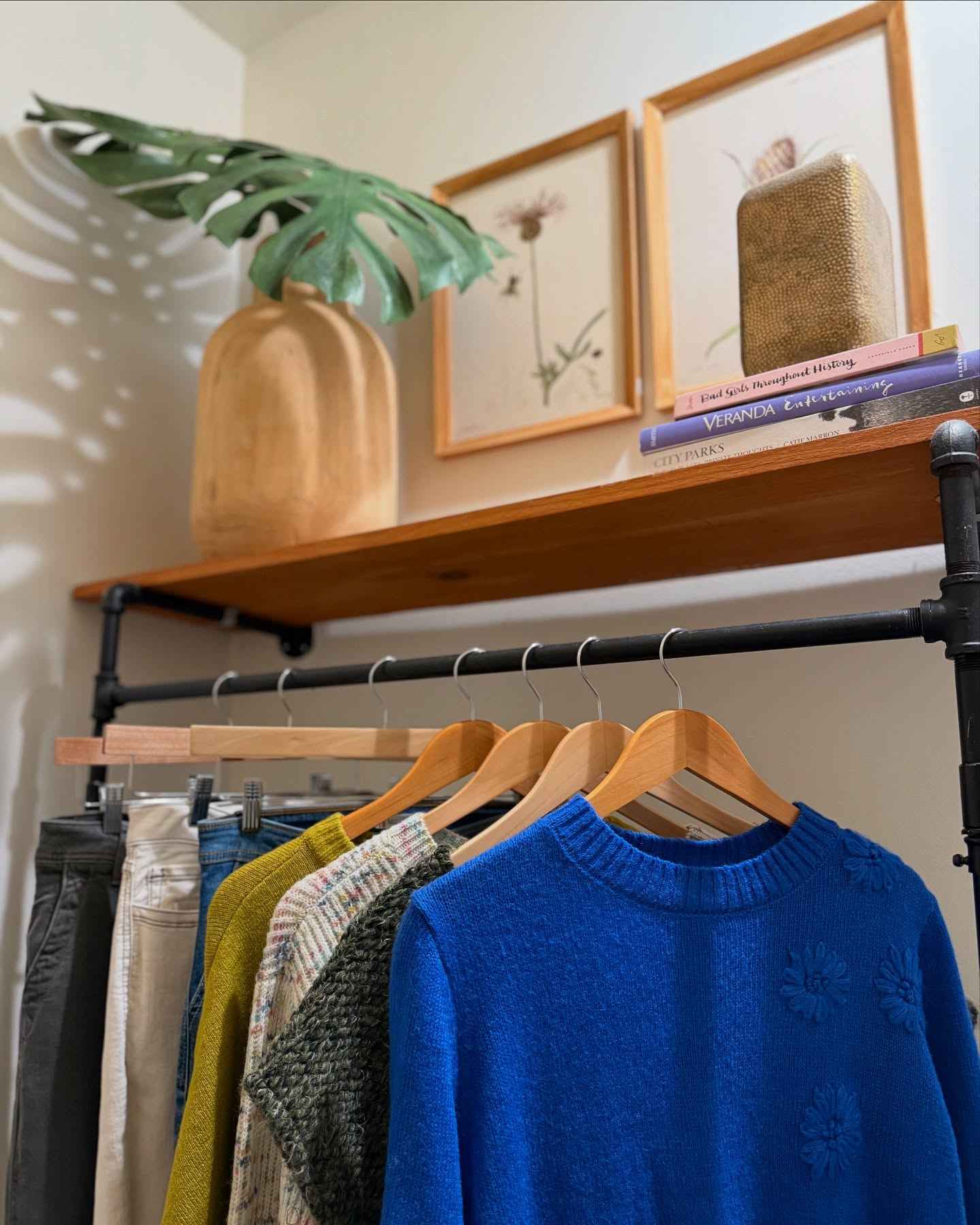 Clothing rack with a blue sweater and various items on a shelf with decor