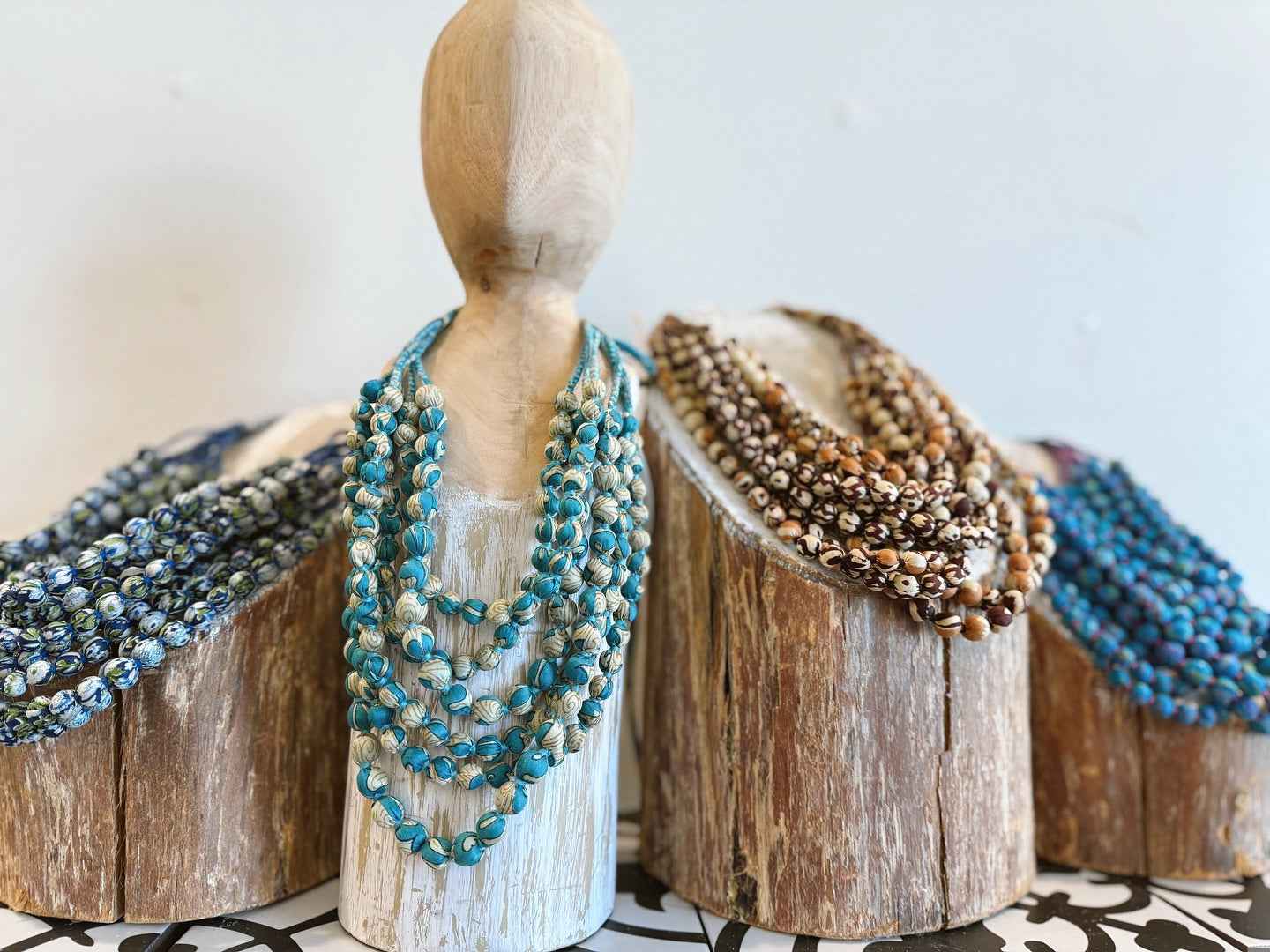 Mannequin wearing multiple beaded necklaces on a wooden block with a light background