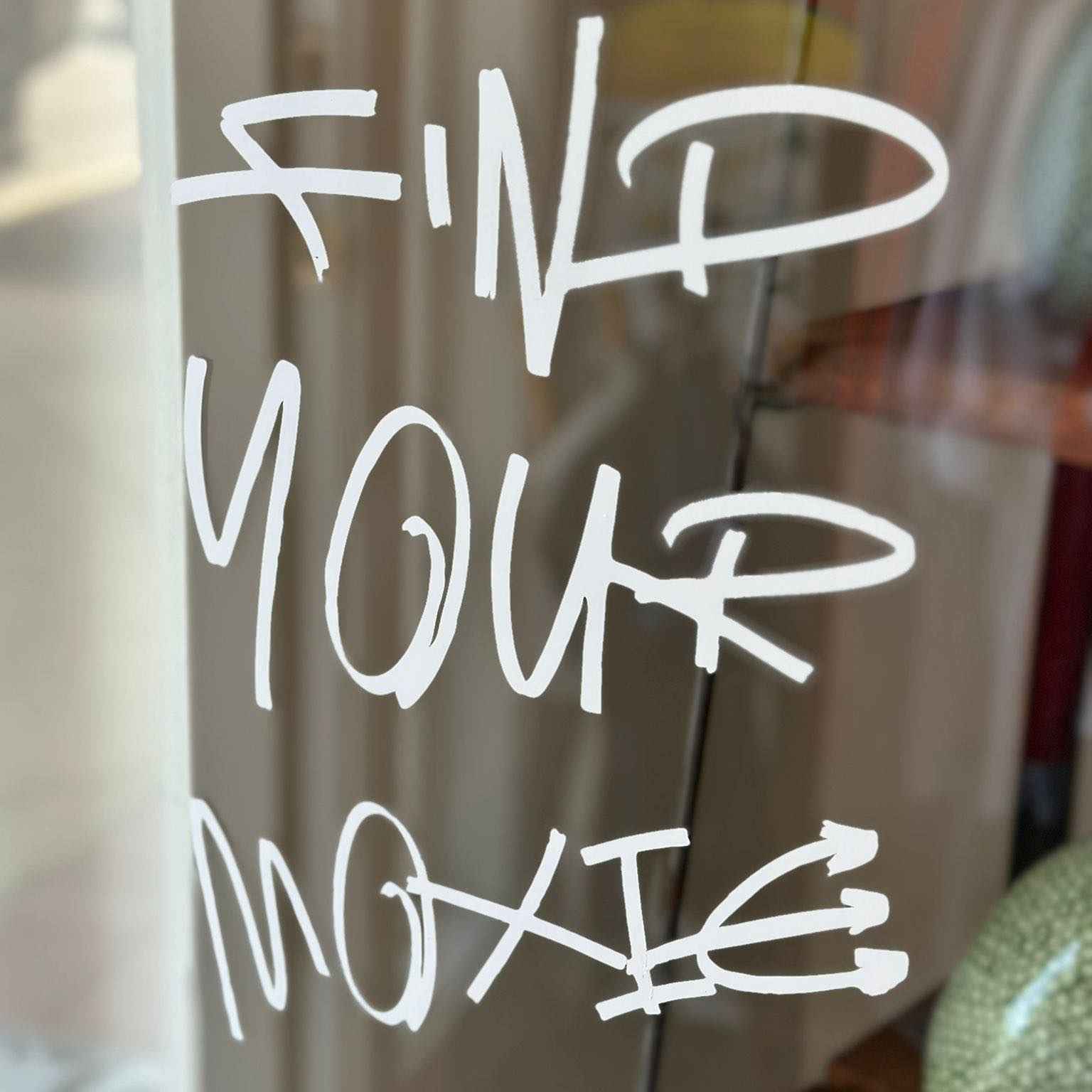 White text 'FIND YOUR MOXIE' on a glass surface with a blurred background