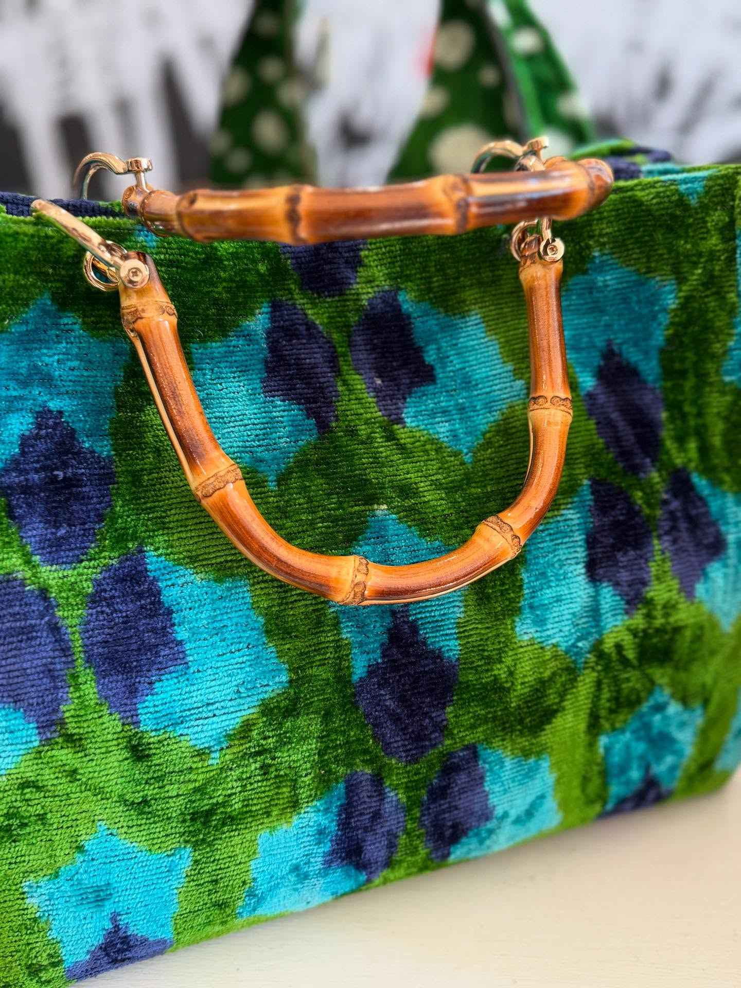 Blue and green patterned handbag with a bamboo handle on a white surface.