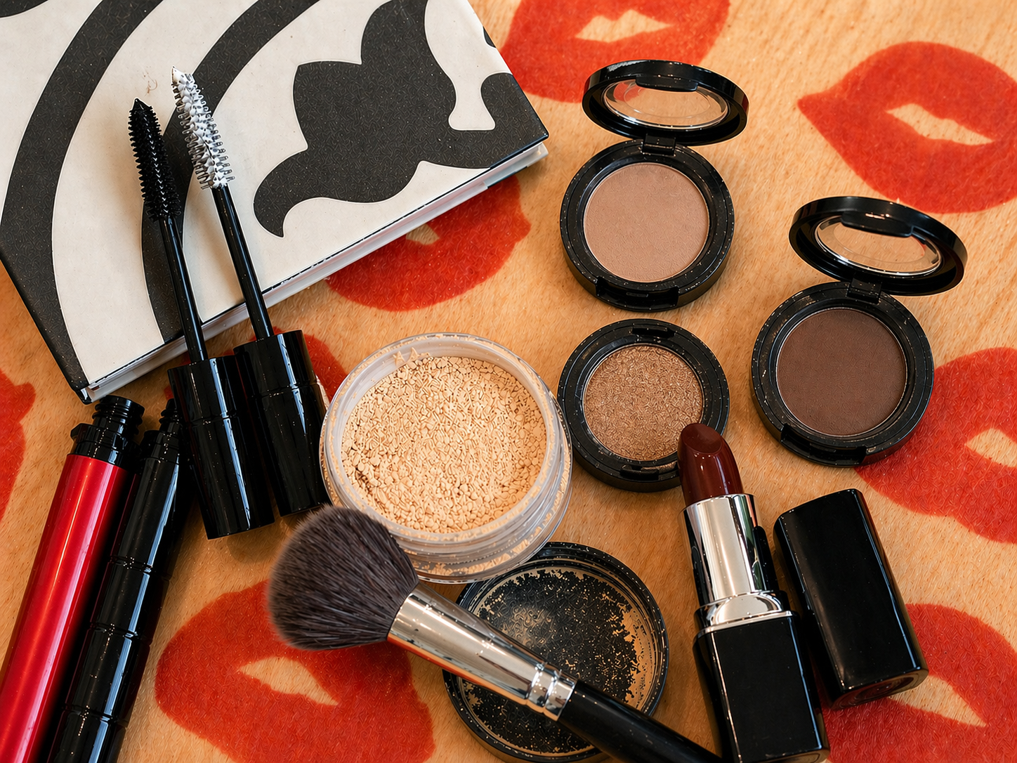 Makeup products including lipsticks, brushes, and compacts on a floral-patterned surface.