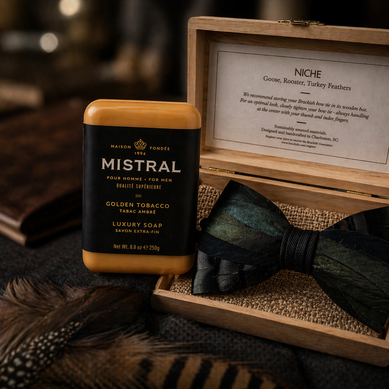 Mistral Golden Tobacco luxury soap with a wooden box containing feathers and a bow tie.