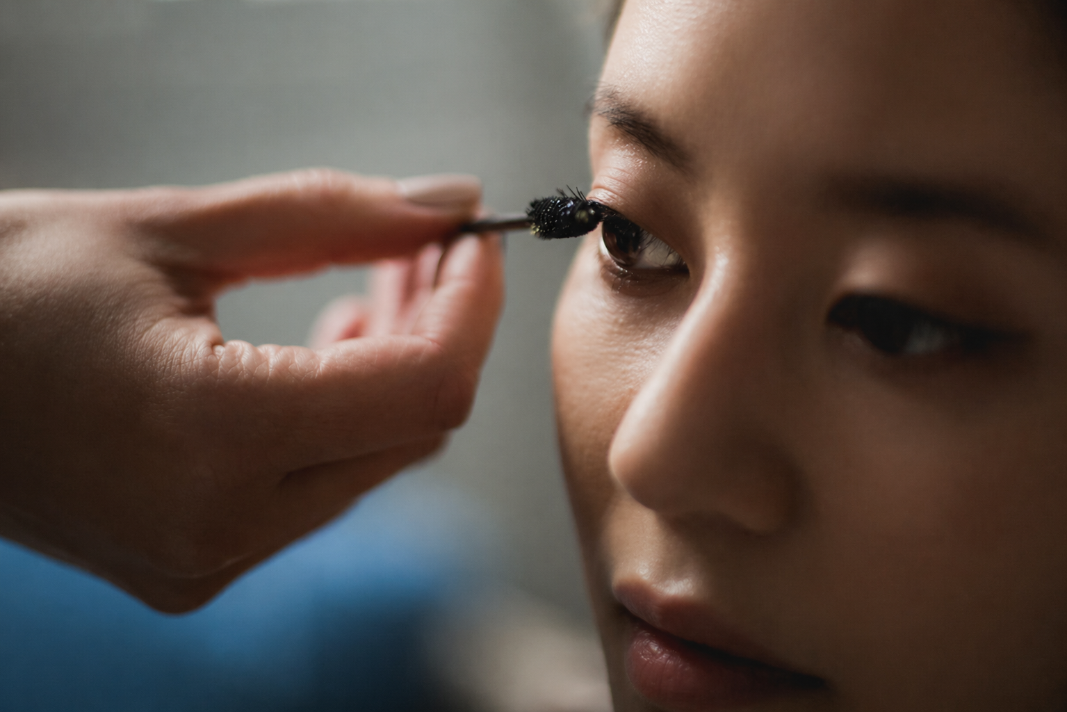 Person applying eyeliner to another person's eye with a brush.