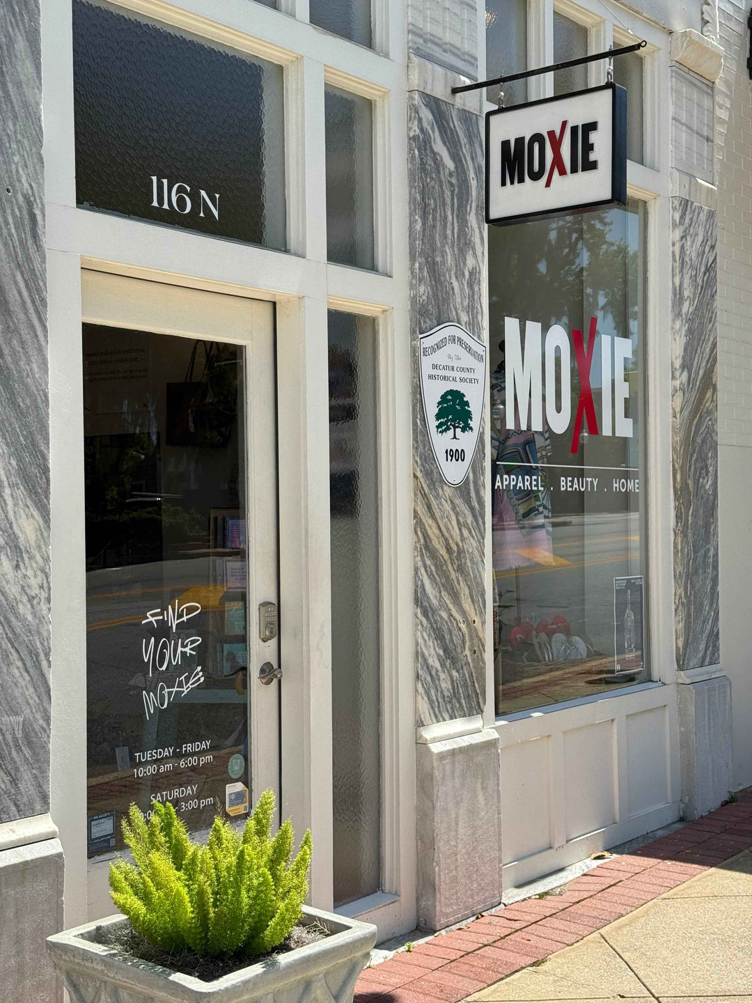 Storefront with 'Moxie' branding and a plant on a pole.