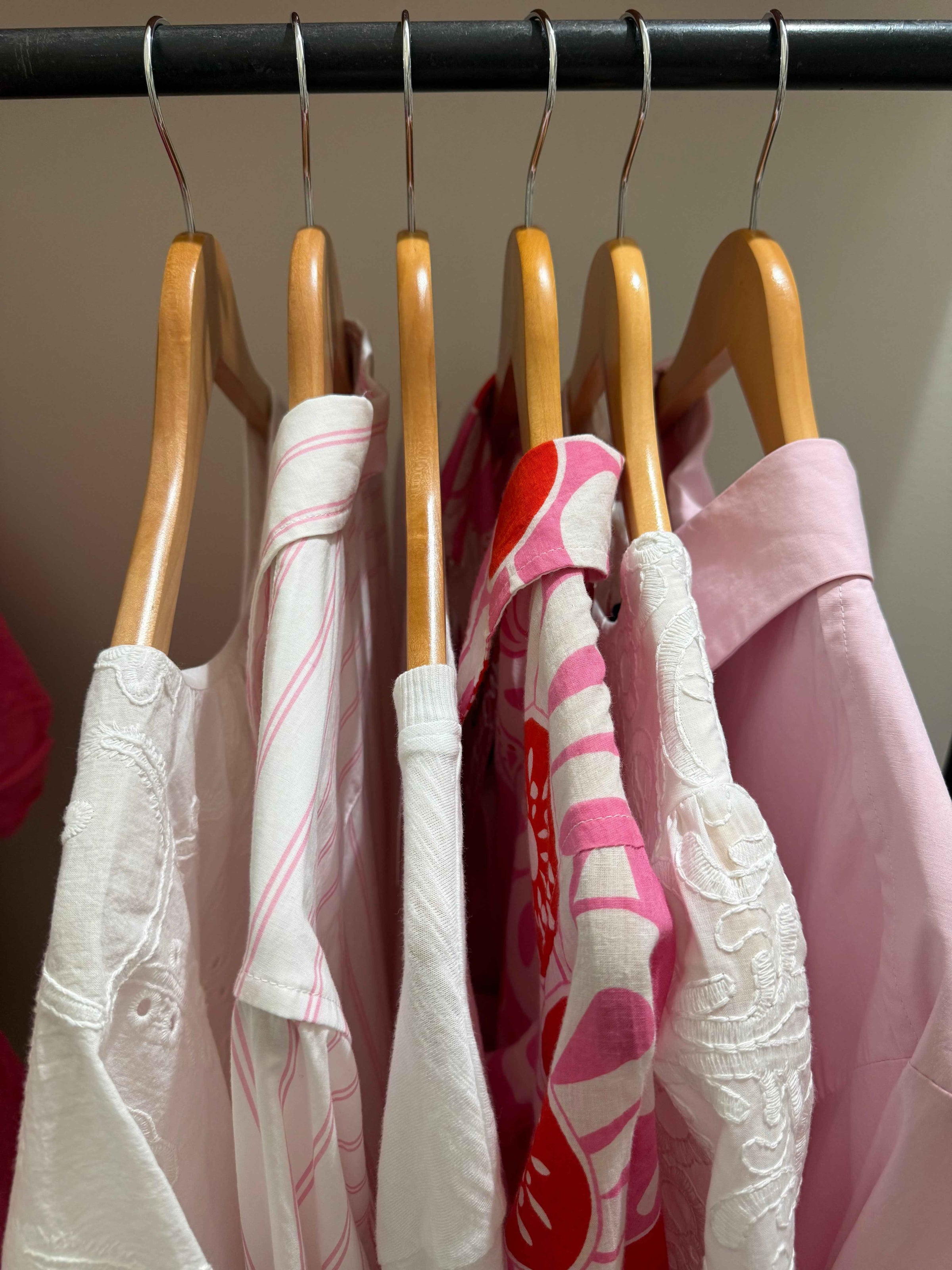 Clothing on a rack with wooden hangers against a neutral background