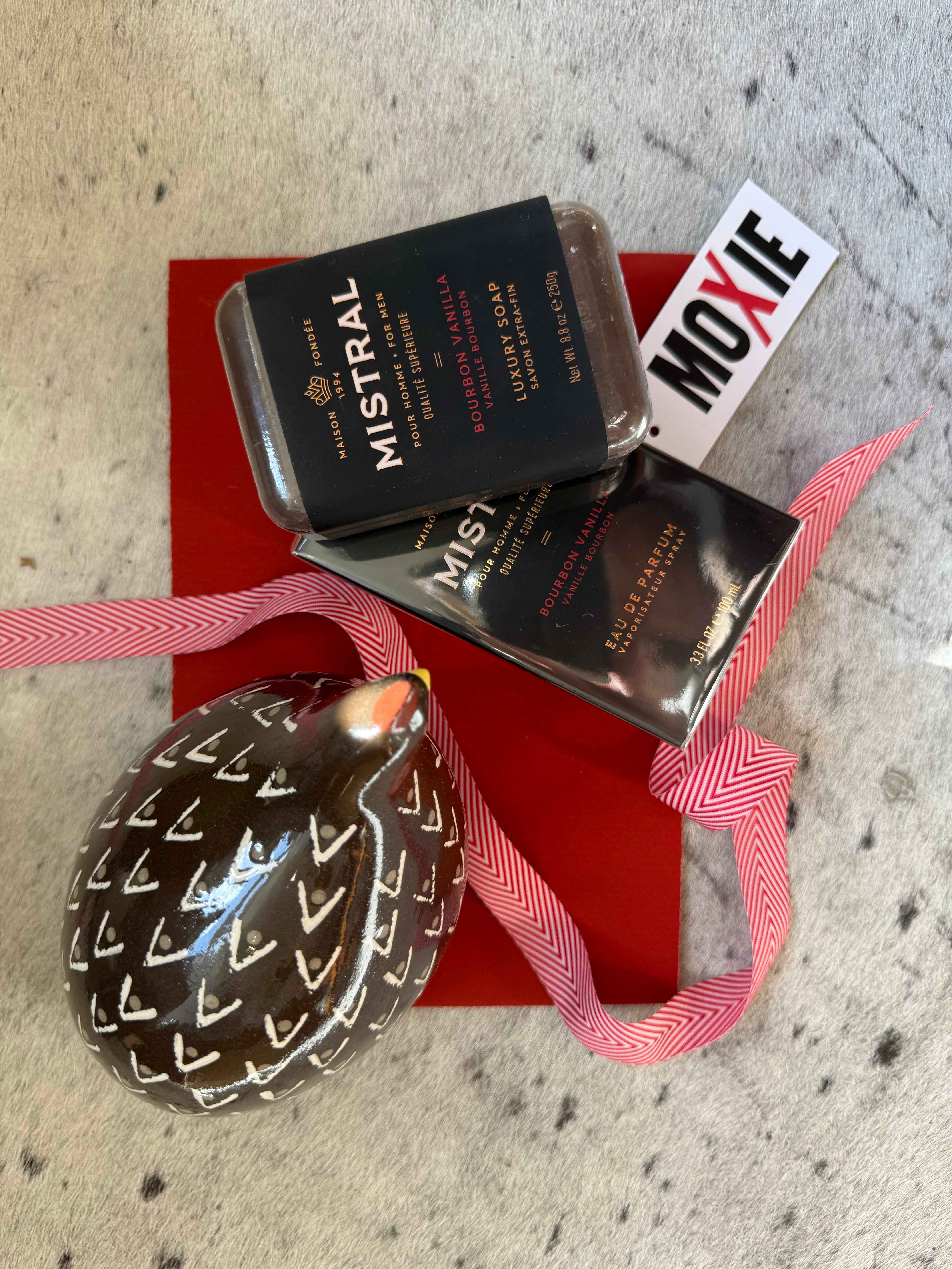 Mistral soap packaging with a decorative egg and red ribbon on a textured surface