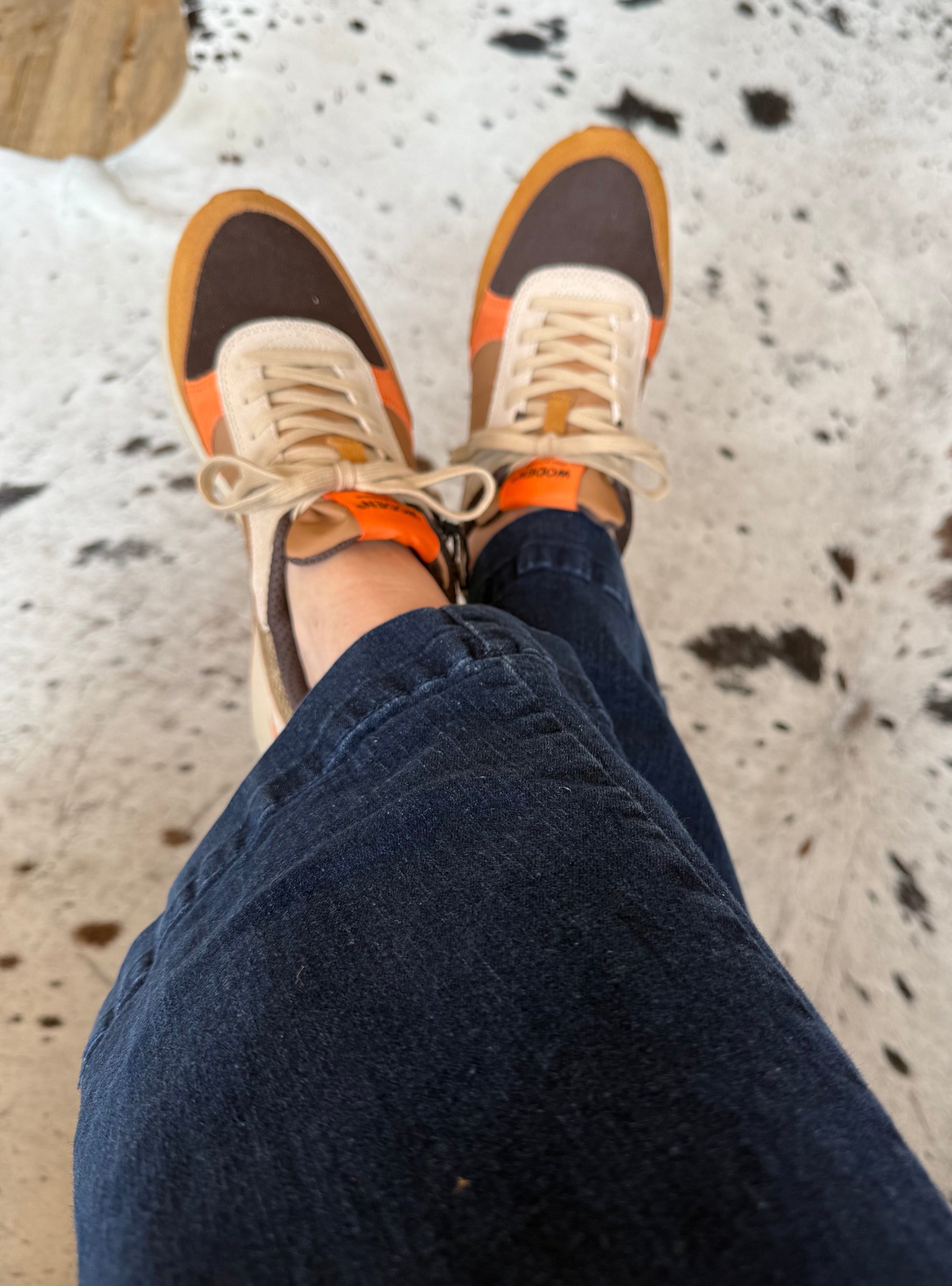 Person wearing orange and beige sneakers with dark blue jeans on a cowhide rug.