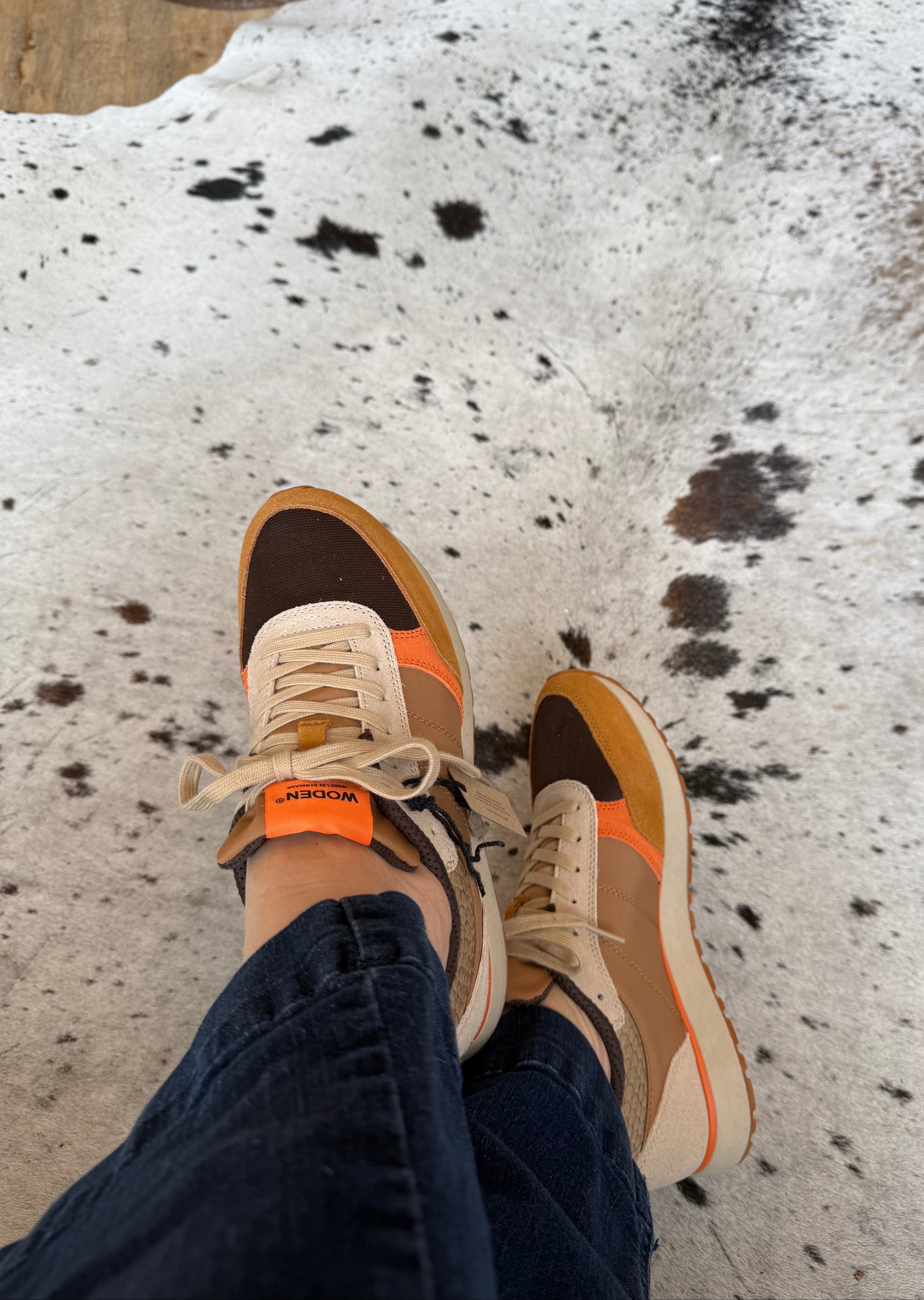 Person wearing brown and orange sneakers on a cowhide rug
