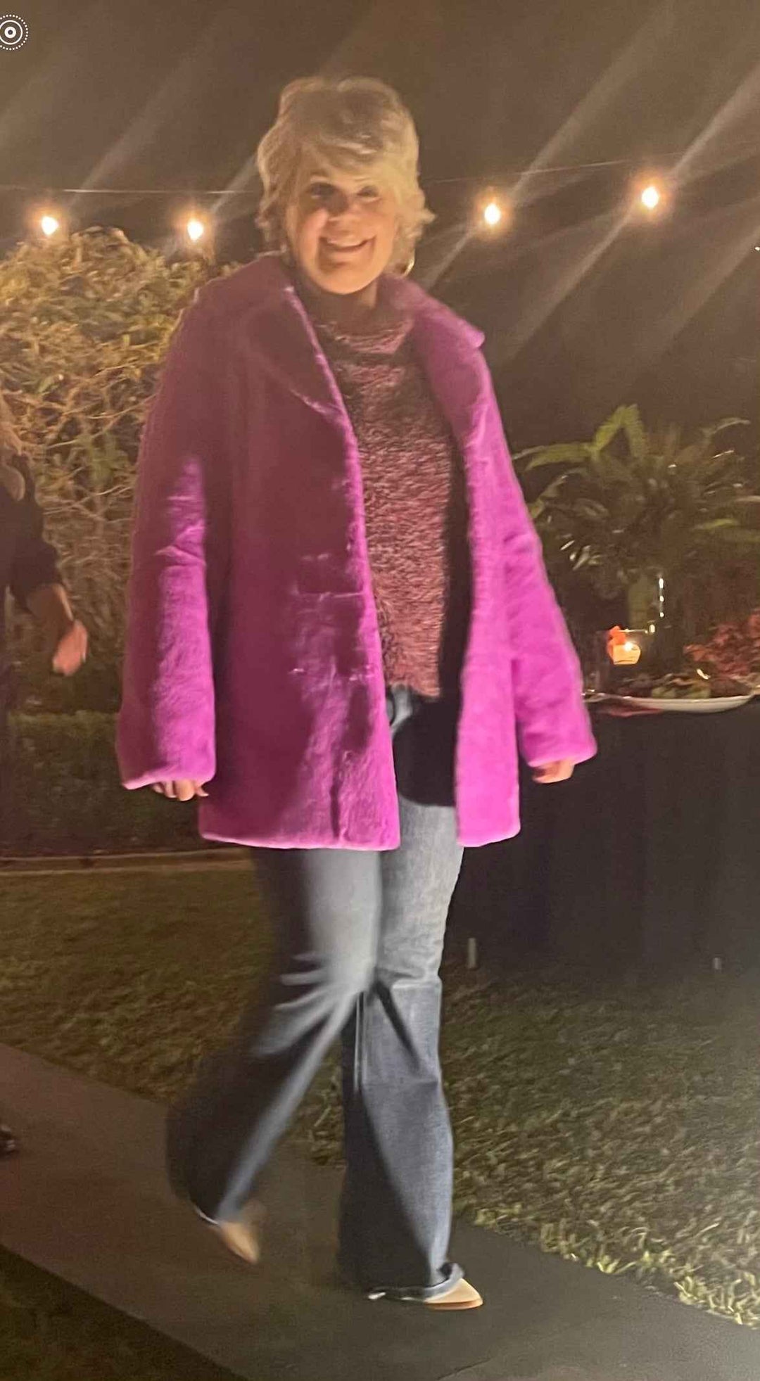Person wearing a purple coat and blue jeans standing outdoors at night.